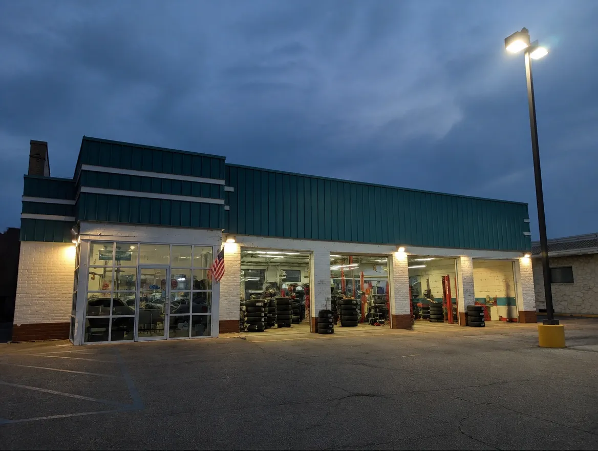 A commercial building at dusk with wall packs lit and a parking lot pole light